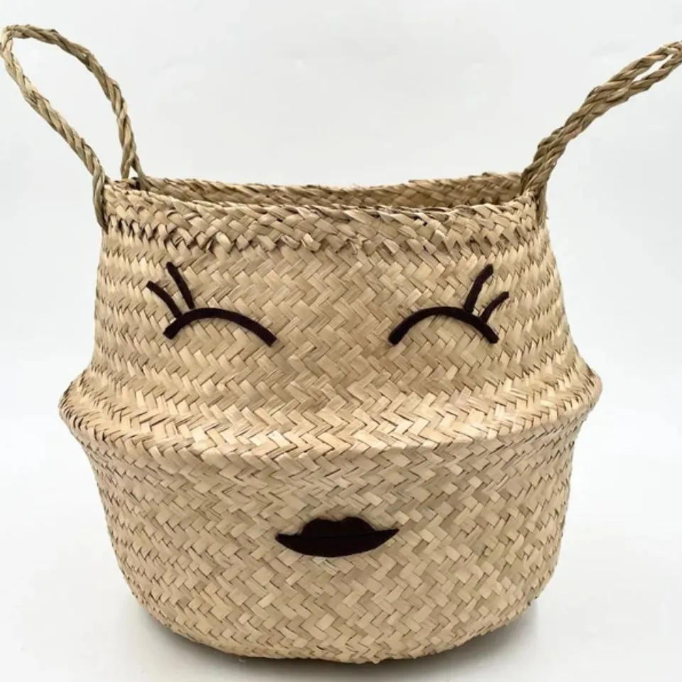 Seagrass belly basket with embroidered winking face and handles, handmade decorative storage by EHM Vietnam.