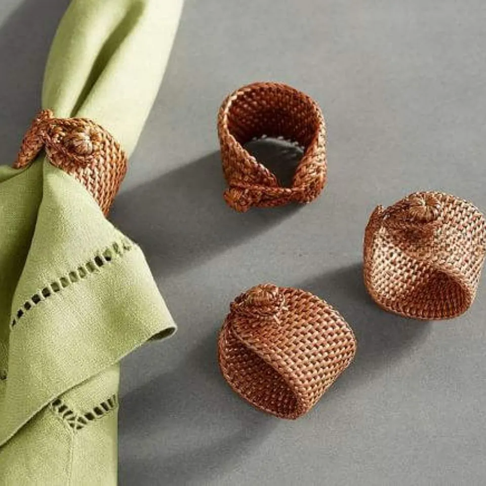 Handcrafted rattan napkin rings with knotted floral detail, displayed with linen napkin for premium tableware presentation.