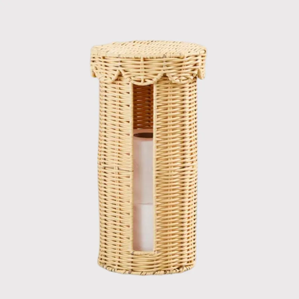 Tall cylindrical rattan toilet roll holder with scalloped lid and front cutout window revealing stacked rolls.